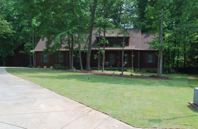 A large lawn in front of a house surrounded by trees.