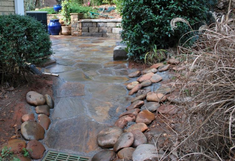 flagstone patio extention with drainage system and rocks on the edging to prevent soil erosion